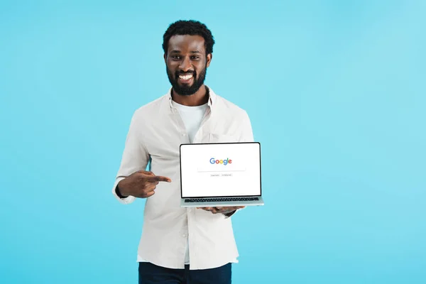 乌克兰 2019年5月17日 微笑的非洲裔美国人指着笔记本电脑与谷歌网站 孤立在蓝色 — 图库照片