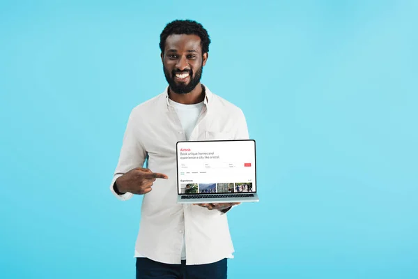 乌克兰 2019年5月17日 微笑的非洲裔美国人指着笔记本电脑与Airbnb网站 孤立在蓝色 — 图库照片