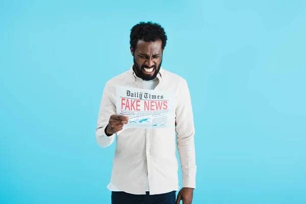 frustrated african american man reading newspaper with fake news isolated on blue