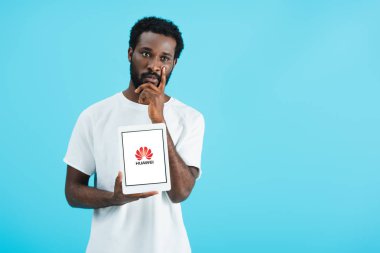 Kiev, Ukrayna - 17 Mayıs 2019: huawei uygulaması ile dijital tablet gösteren düşünceli Afrikalı-Amerikalı adam, mavi izole