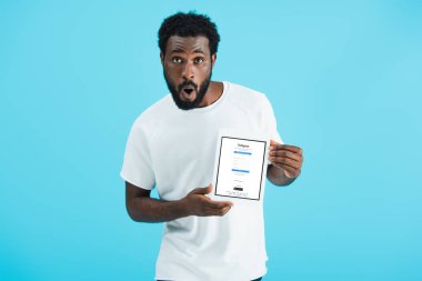 Kiev, Ukrayna - 17 Mayıs 2019: Instagram uygulaması ile dijital tablet gösteren afro-amerikan adam şaşırttı, mavi izole