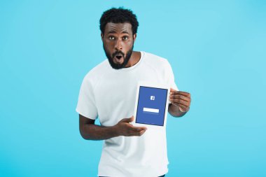 Kiev, Ukrayna - 17 Mayıs 2019: facebook uygulaması ile dijital tablet gösteren şok Afrikalı Amerikalı adam, mavi izole
