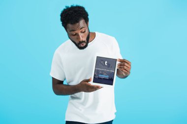 Kiev, Ukrayna - 17 Mayıs 2019: tumblr uygulaması ile dijital tablet bakarak şok Afrikalı Amerikalı adam, mavi izole