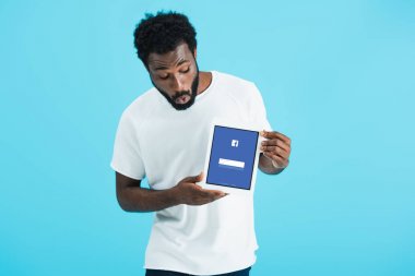 Kiev, Ukrayna - 17 Mayıs 2019: facebook uygulaması ile dijital tablet bakarak şok Afrikalı Amerikalı adam, mavi izole
