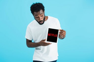 Kiev, Ukrayna - 17 Mayıs 2019: netflix uygulaması ile dijital tablet bakarak şok Afrikalı Amerikalı adam, mavi izole