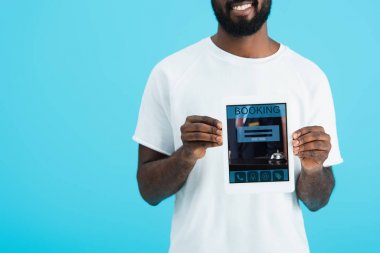 mavi izole rezervasyon uygulaması ile dijital tablet gösteren Afrikalı Amerikalı adam kırpılmış görünümü