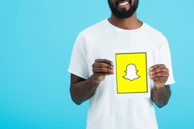 Kiev, Ukrayna - 17 Mayıs 2019: Snapchat uygulaması ile dijital tablet gösteren Afrikalı Amerikalı adamın kırpılmış görünümü, mavi izole