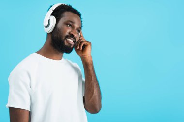 young african american man listening music with headphones, isolated on blue clipart