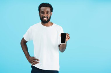 beyaz ekranlı akıllı telefonu işaret eden gülümseyen afro-amerikan adam, mavi izole
