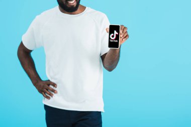 Kiev, Ukrayna - 17 Mayıs 2019: Tik Tok uygulaması ile akıllı telefon gösteren Afrikalı-Amerikalı adamın kırpılmış görünümü, mavi izole