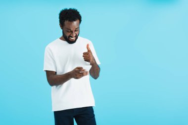 akıllı telefon kullanarak ok işareti ile gülümseyen afrikalı amerikalı adam, mavi izole