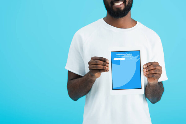 KYIV, UKRAINE - MAY 17, 2019: cropped view of african american man showing digital tablet with twitter app, isolated on blue