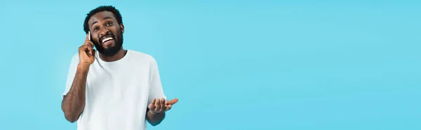 スマートフォンで話すシュラッグジェスチャーを持つ笑顔のアフリカ系アメリカ人男性 青で孤立 — ストック写真