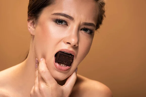 ベージュで孤立した手で顔を持つ口の中のチョコレート片を持つ女性を強調する — ストック写真