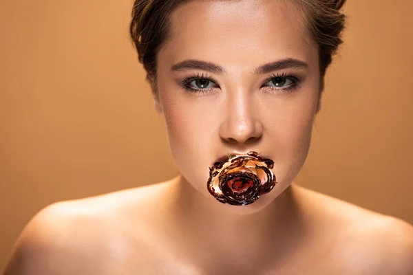 年轻的裸体女人抱着玫瑰在嘴上覆盖着融化的巧克力孤立在米色 — 图库照片