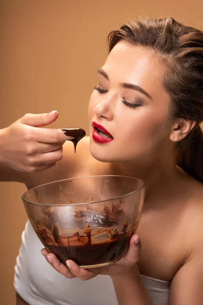 美丽的女人与红嘴唇吃融化的巧克力从碗隔离在米色 — 图库照片