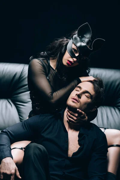 黒の革のソファに触れるBdsmの衣装とマスクのセクシーな女性 — ストック写真
