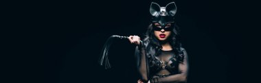 panoramic shot of sexy young brunette woman in bdsm costume and mask with leather flogging whip isolated on black clipart
