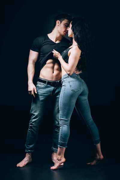 barefoot couple in denim undressing and kissing isolated on black 