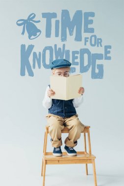ahşap merdivenlerde oturan sevimli çocuk ve bilgi için zaman ile gri arka plan üzerinde kitap okuma 