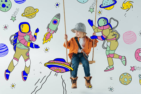 cute kid in jeans and orange shirt sitting on swing and looking at fairy space with astronauts illustration on grey background