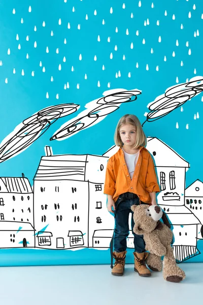 建物のイラストの上に雨と青い背景にテディベアを保持して動揺と愛らしい子供 — ストック写真