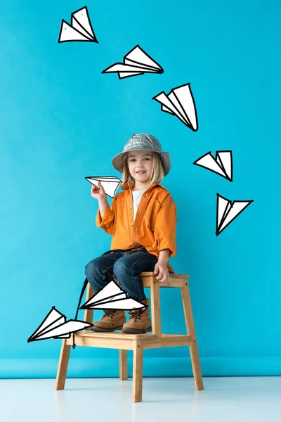 階段に座って妖精の紙飛行機で遊ぶジーンズとオレンジ色のシャツの子供 — ストック写真