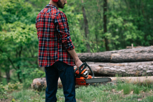 cropped view of lumberjack in checkered shirt holding chainsaw in forest