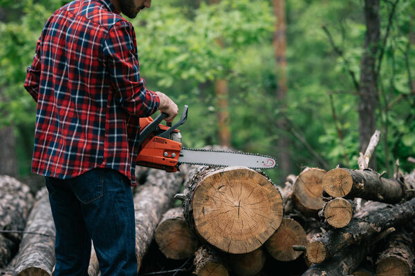 partial view of lumberjack cutting trunk with chainsaw in forest