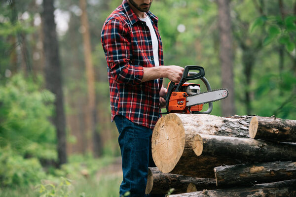 cropped view of lumberjack cutting round timbers with chainsaw in forest