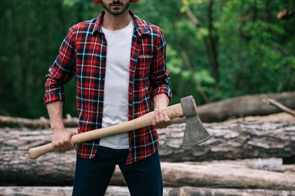 cropped view of lumberman in plaid shirt holding axe in forest