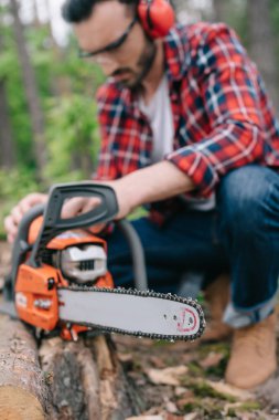 selective focus of lumberjack repairing electric chainsaw in forest clipart