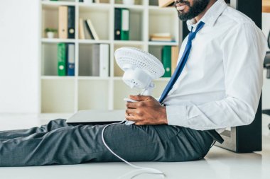 ofiste ısı muzdarip iken katta oturan ve elektrik fan tutarak Afrikalı Amerikalı işadamı kırpılmış görünümü