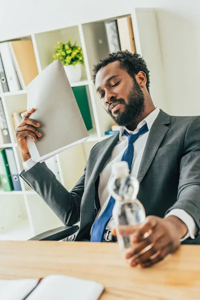 Hombre Negocios Afroamericano Agotado Sosteniendo Botella Agua Carpeta Mientras Sufre —  Fotos de Stock