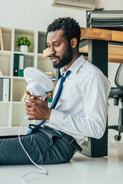 Afrykański Amerykański Biznesmen Trzymający Wentylator Elektryczny Siedząc Podłodze Cierpiący Letnie — Zdjęcie stockowe