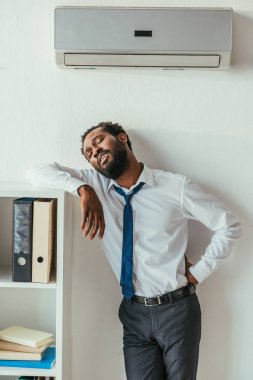 yorgun afro-amerikan işadamı klima altında duran ve kalça el tutarak