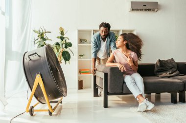 yorgun Afro-Amerikan erkek ve kadın elektrik fan üfleme önünde yaz acı