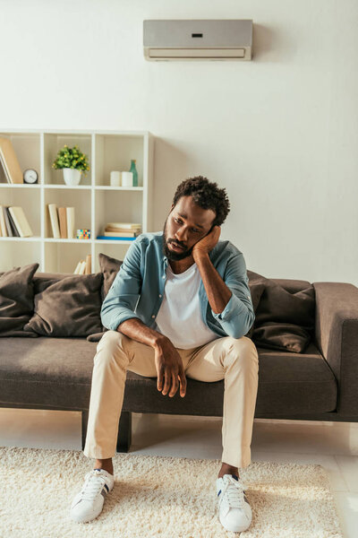 exhausted african american businessman sitting on sofa and suffering from summer heat
