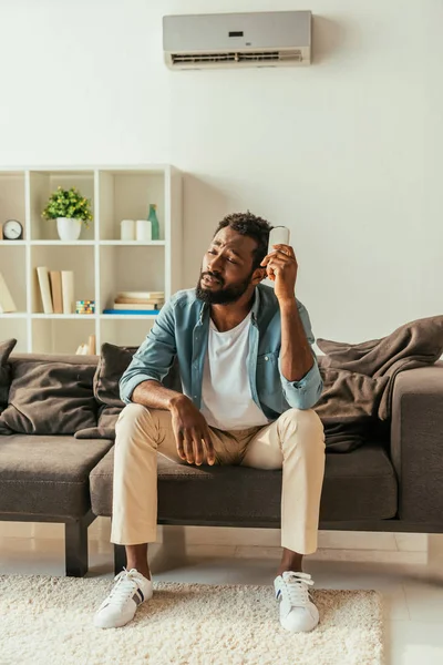 Exhausted African American Man Holding Air Conditioner Remote Controller While — Stock Photo, Image