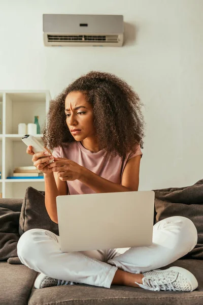 Elégedetlen Afro Amerikai Aki Légkondicionáló Távirányító Ülve Kanapé Laptop — Stock Fotó