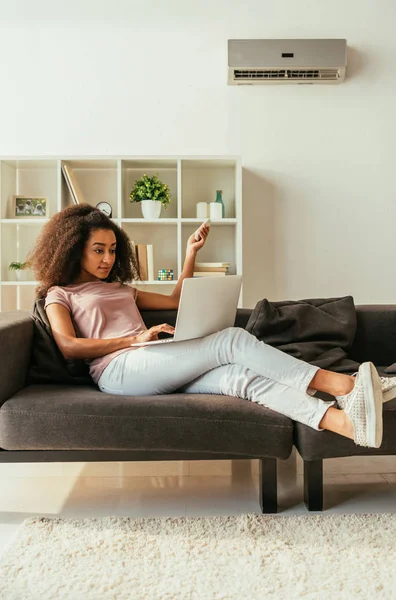 Pretty African American Woman Using Laptop Holding Air Conditioner Remote — Stock Photo, Image