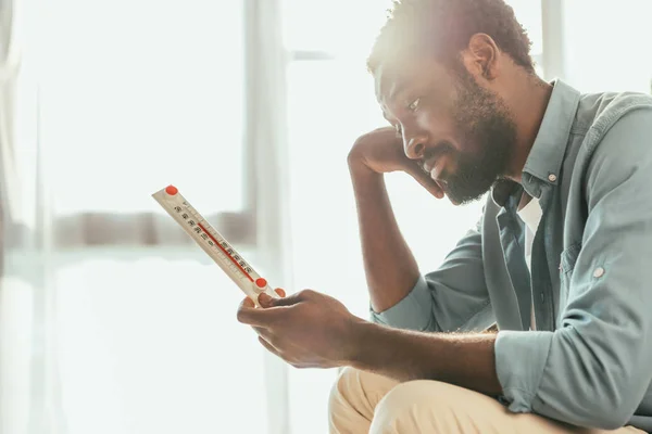 Infeliz Afroamericano Hombre Mirando Termómetro Mientras Sufre Calor Verano Casa —  Fotos de Stock