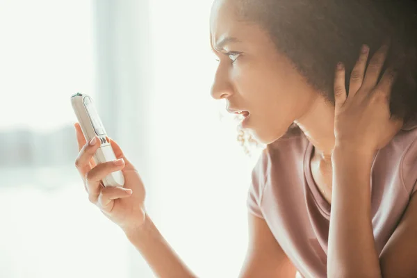 Shocked African American Woman Looking Air Conditioner Remote Controller While — Stock Photo, Image