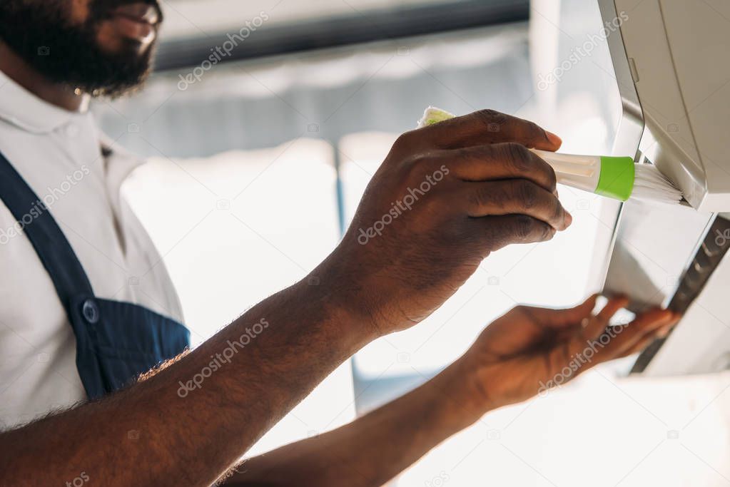 cropped view of african american repairman cleaning air conditioner with brush