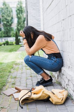 kitaplar arasında duvara yakın oturan tulum içinde hayal kırıklığına uğramış ve esmer genç 