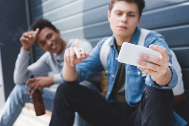 gülümseyen, sigara içen, bira tutan ve selfie çeken arkadaşların seçici odak noktası 