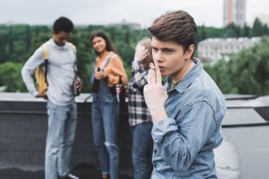 selective focus of teen smoking cigarette and looking away  clipart