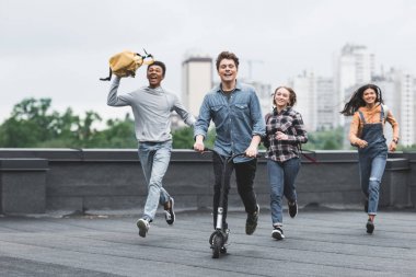çatıda çalışan ve scooter sürme eğlenceli ve gülümseyen gençler 