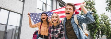 mutlu gençlerin panoramik çekim gülümseyerek, Amerikan bayrağı tutarak ve kameraya bakarak 