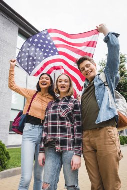mutlu gençler gülümseyerek, Amerikan bayrağı tutarak ve kameraya bakarak 